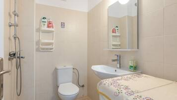 A bathroom with a toilet, shower, sink, and a mirror.