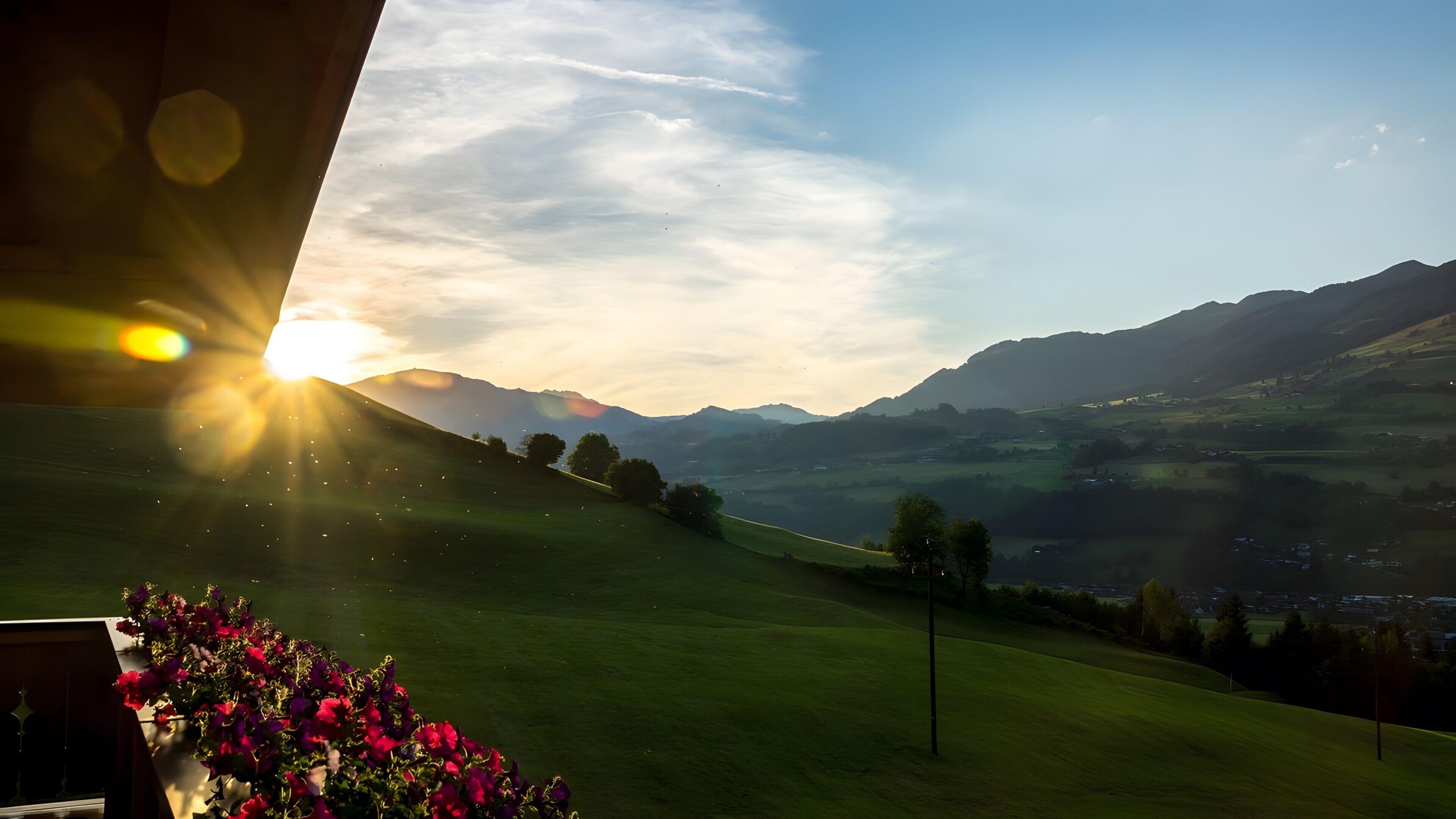 A view of a green landscape with mountains in the distance and a bright sun in the sky.