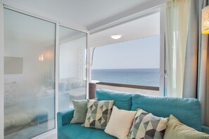 Un balcon avec vue sur la mer, un canapé bleu orné de coussins à motifs et une cloison en verre.