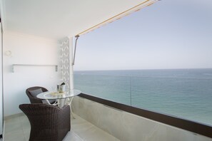 Een balkon met rieten stoelen, een glazen tafel en uitzicht op zee.