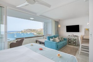 Habitación de hotel con balcón, cama, sofá, televisión y vista al mar.