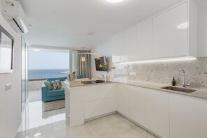 Een moderne keuken met uitzicht op zee, witte kastjes, een inbouwspoelbak en een zithoek met een blauwe bank.