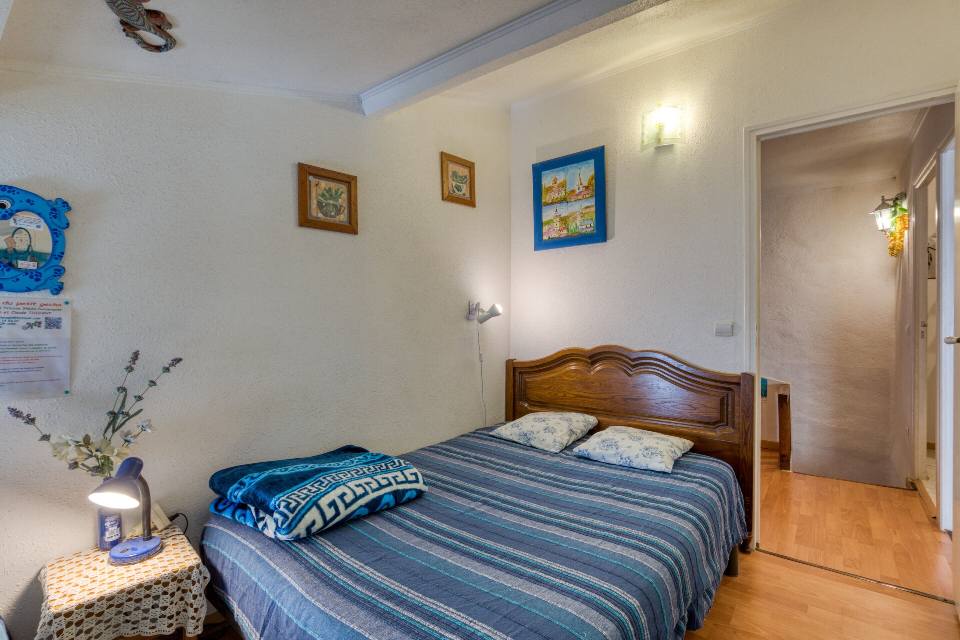 Een slaapkamer met een houten bed, een nachtkastje met een lamp en een wand met ingelijste foto's.