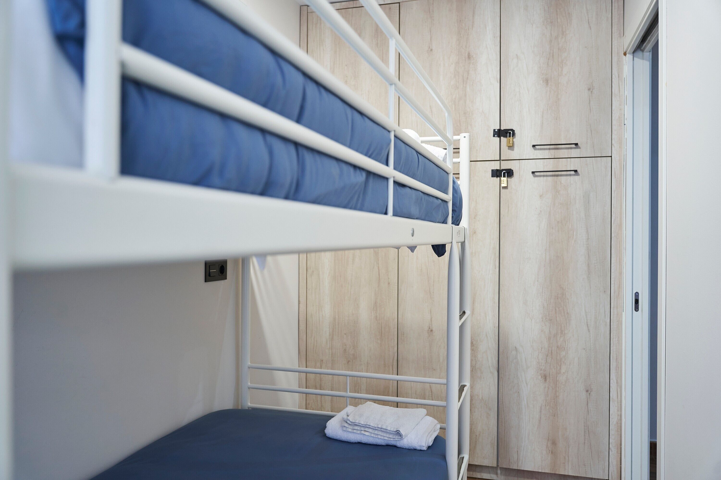 Un lit superposé avec un matelas bleu, une couverture blanche et une armoire en bois à deux portes.