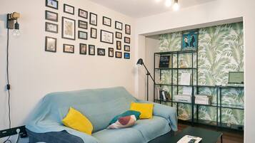 A room with a light blue sofa, yellow pillows, a black coffee table, a bookshelf, and a wall with framed pictures.