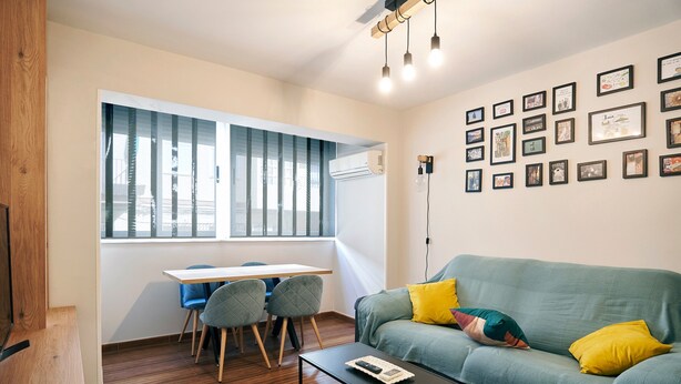 Ein Wohnzimmer mit Sofa, Couchtisch, Esstisch mit Stühlen und einer Wand mit gerahmten Bildern.