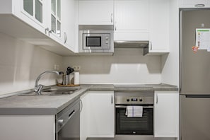 A modern kitchen with white cabinetry, stainless steel appliances, a built-in oven, and a refrigerator.