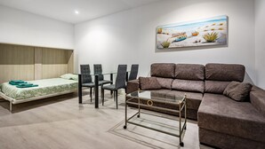A modern room with a bed, a sofa, a glass coffee table, and a dining table with chairs.