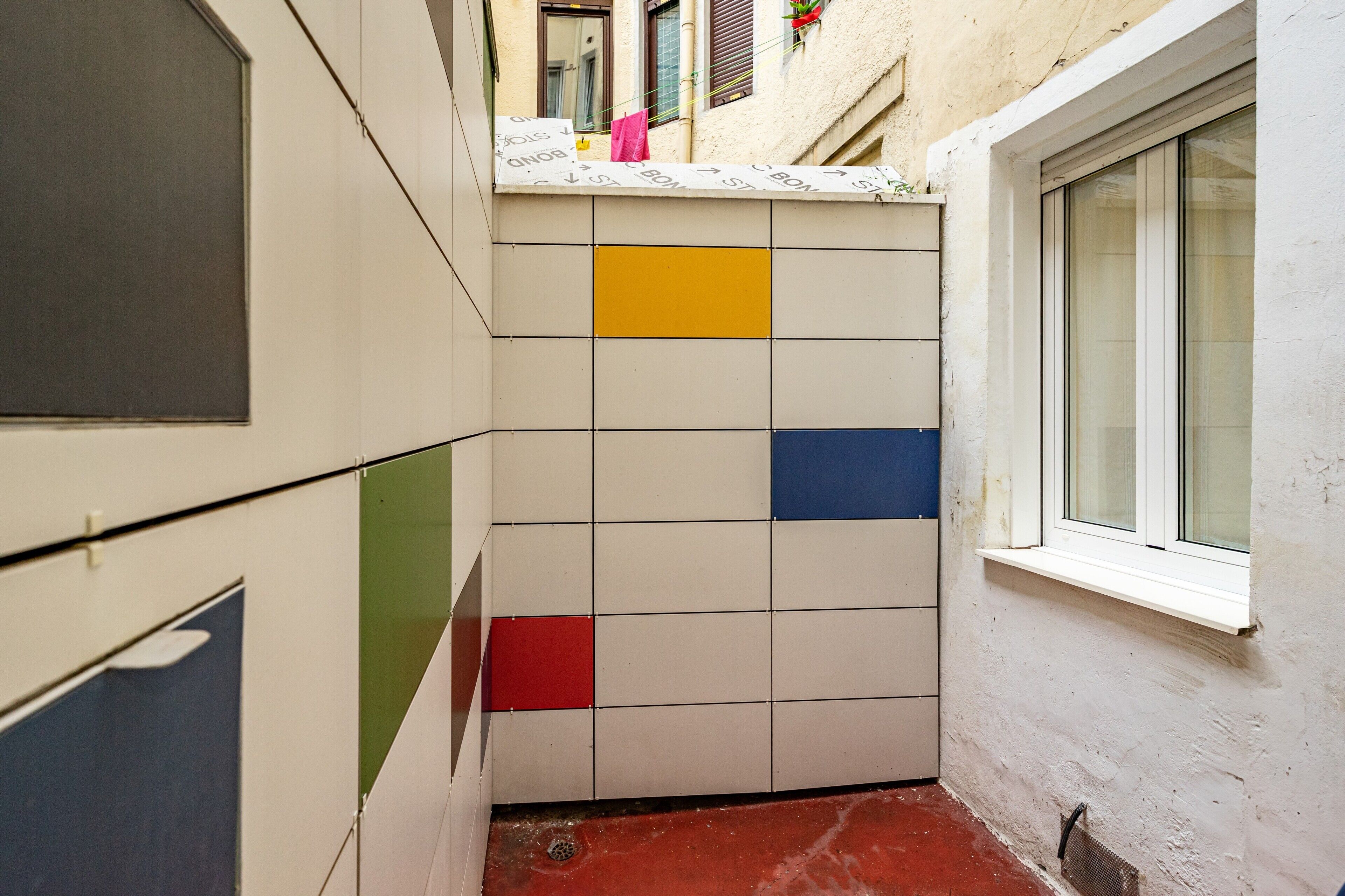 Un pasillo estrecho con paredes de baldosas, una ventana y suelo rojo.