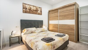 A bedroom with a bed, bedside table, lamp, artwork, wardrobe, and a shelf unit.