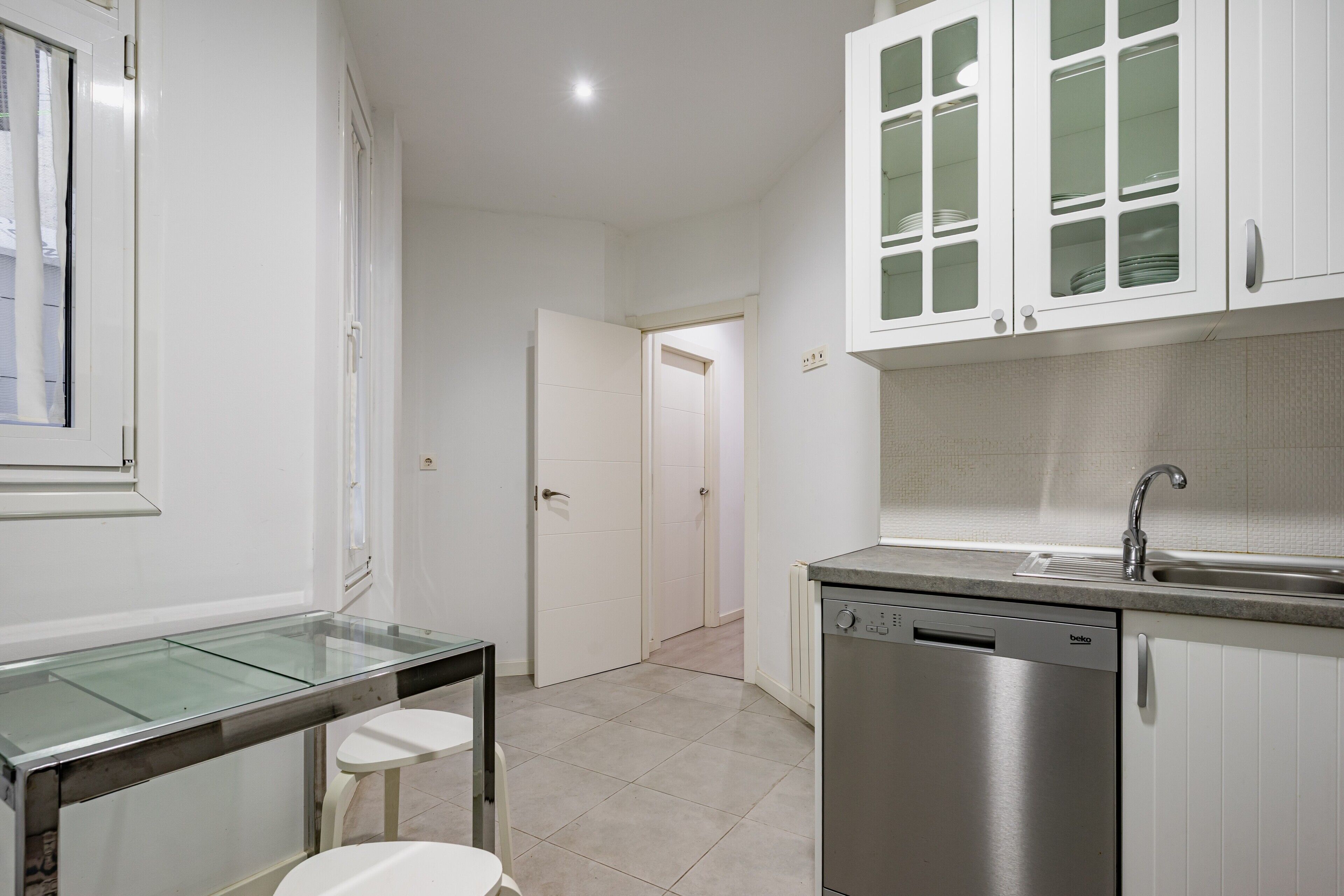 A modern kitchen with white cabinets, a dishwasher, and a glass-top table.