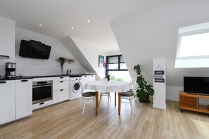A modern kitchen with white cabinetry, a dining table, and a flat-screen TV.