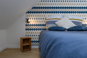 Une chambre avec un papier peint à motifs, un lit avec une literie bleue et une petite table de chevet en bois.