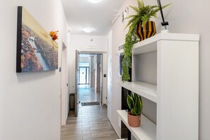 Un corridoio con un quadro, una pianta in vaso e uno scaffale con una pianta.