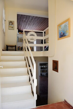 Eine Treppe mit weißen Geländern führt zu einem Schlafzimmer auf dem Dachboden, das einen Holzboden hat.