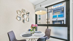 Ein moderner Essbereich mit einem runden Tisch, vier Stühlen, einer Blumenvase und einem großen Fenster mit Blick auf Gebäude.