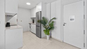 Eine moderne Küche mit weißen Schränken, einem Edelstahlkühlschrank, einer Waschmaschine und einem Blumentopf.