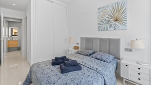 Ein Schlafzimmer mit einem Bett, Kissen, einem Nachttisch, einer Lampe, einem Wandbild und einem Kleiderschrank.