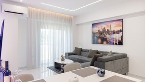 Un salon moderne avec un canapé gris, une table basse en verre et un tableau représentant un paysage urbain accroché au mur.