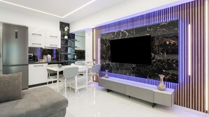 Un salon moderne doté d’un téléviseur à écran plat, d’un canapé, d’une table à manger et d’un coin cuisine.