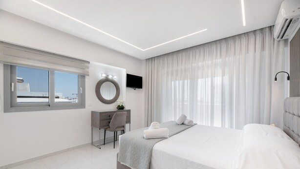Une chambre d’hôtel moderne dotée d’un grand lit, d’un bureau, d’une chaise, d’un miroir rond, d’un téléviseur à écran plat et d’une fenêtre avec des rideaux.