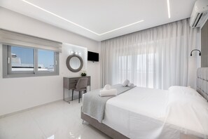 Habitación de hotel moderna con una cama grande, un escritorio, una silla, un espejo redondo, un televisor de pantalla plana y un ventanal con cortinas.