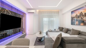 Une chambre d’hôtel moderne équipée d’un téléviseur à écran plat, d’un canapé, d’un lit, d’un coin repas et d’une grande fenêtre avec des rideaux.