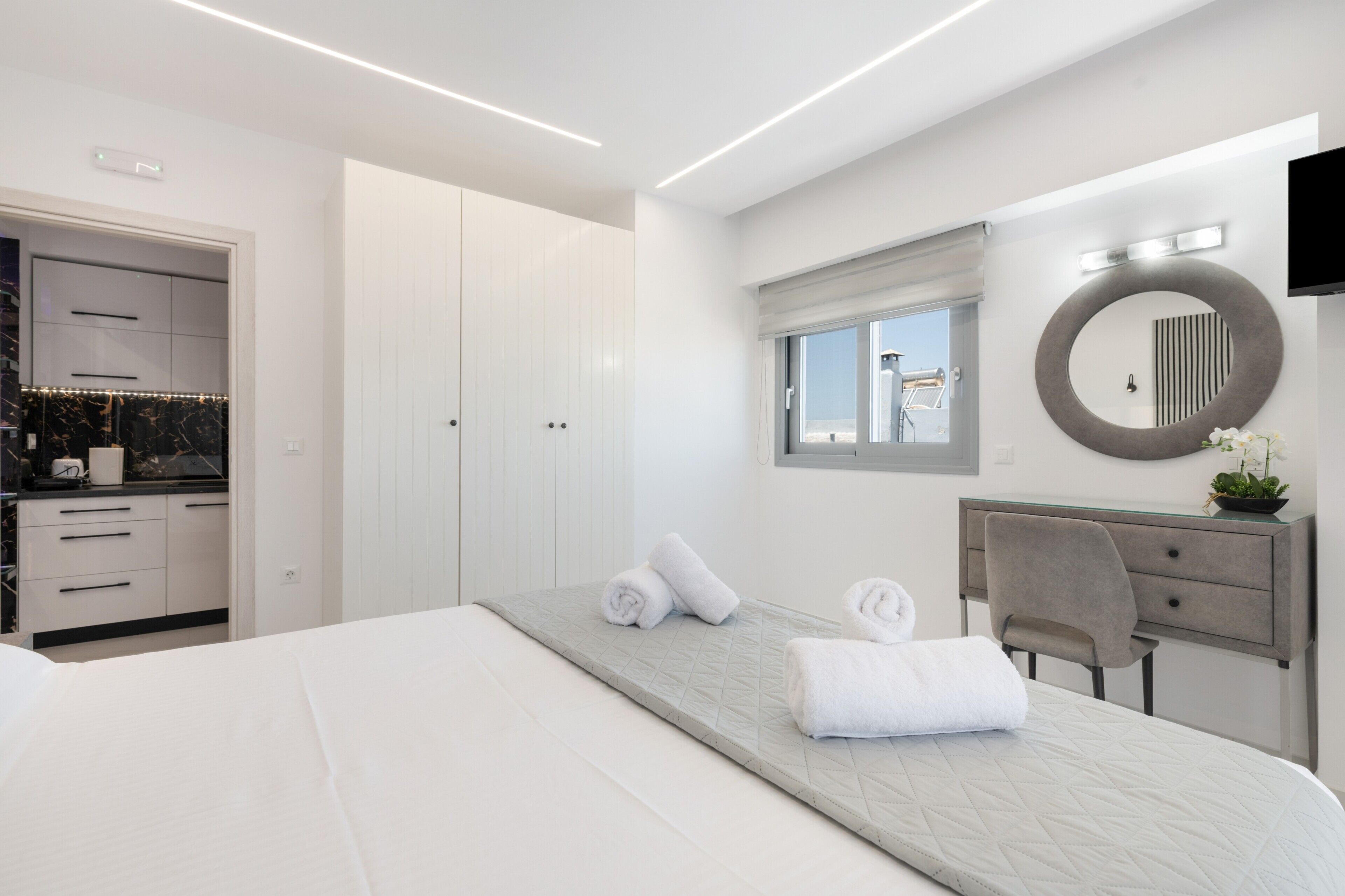 Een moderne hotelkamer met een bed, een bureau, een stoel, een ronde spiegel en een raam.