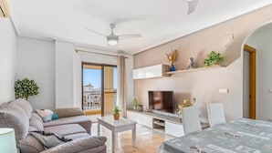 Uma sala de estar moderna com sofá, televisão, mesa de jantar e varanda com vista.