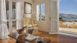 Una habitación con una mesa de madera, un sillón color crema, un sofá y vistas al mar.