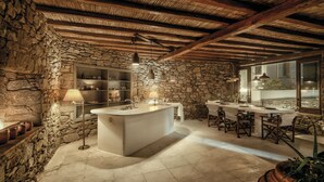 Un interior rústico con pared de piedra, una isla central con lavamanos y una zona de comedor con sillas y mesas.