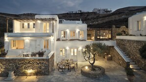 Un edificio moderno blanco con varios niveles, mesas al aire libre y una pared de piedra.