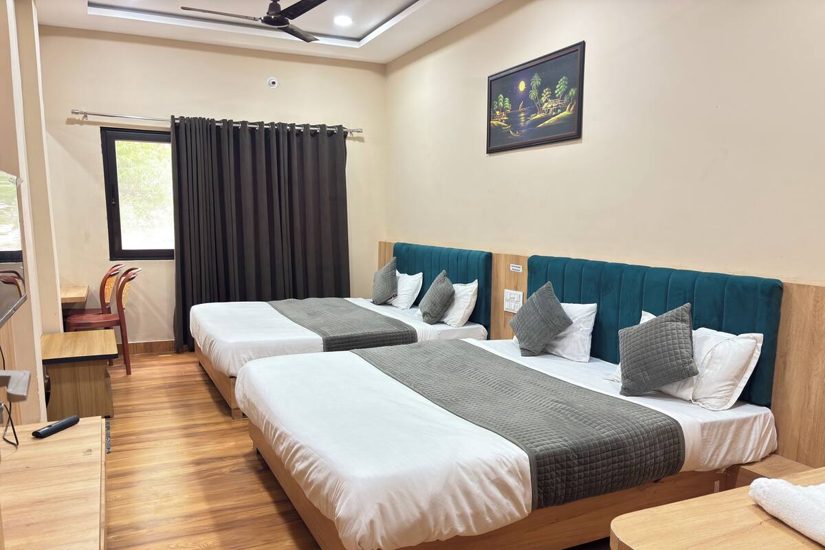 Habitación de hotel con dos camas, un escritorio, una silla, un ventilador de techo y un cuadro en la pared.