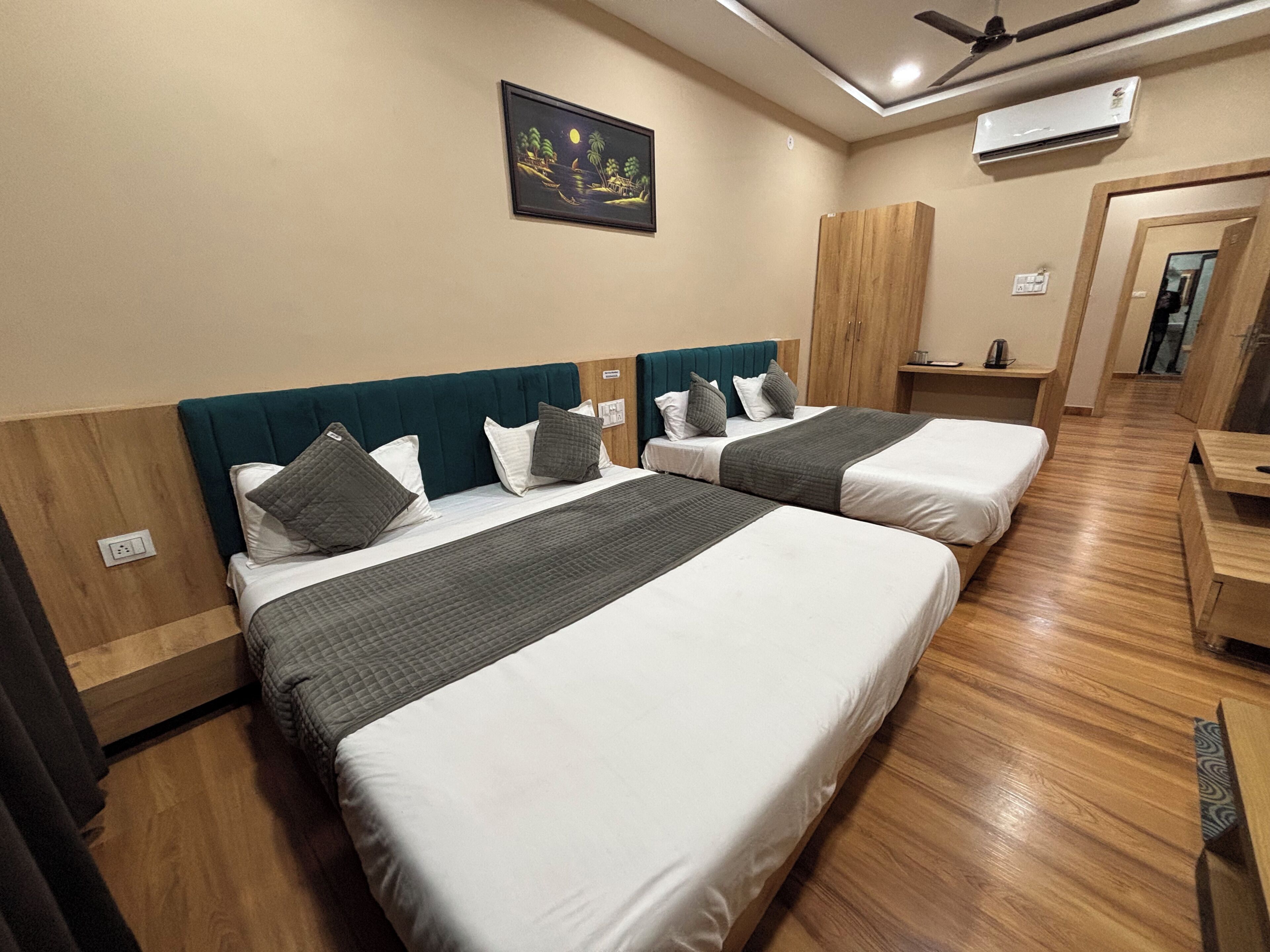 A hotel room with two beds, a ceiling fan, an air conditioning unit, and a painting on the wall.