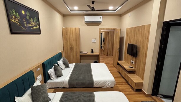 A hotel room with two beds, a ceiling fan, an air conditioning unit, a TV, and a painting on the wall. - Hotel Bhavya Ujjain (Ujjain)