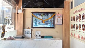 A reception desk with a ceiling fan, a wall-mounted calendar, and a wall with religious icons. - Hotel Bhavya Ujjain (Ujjain)