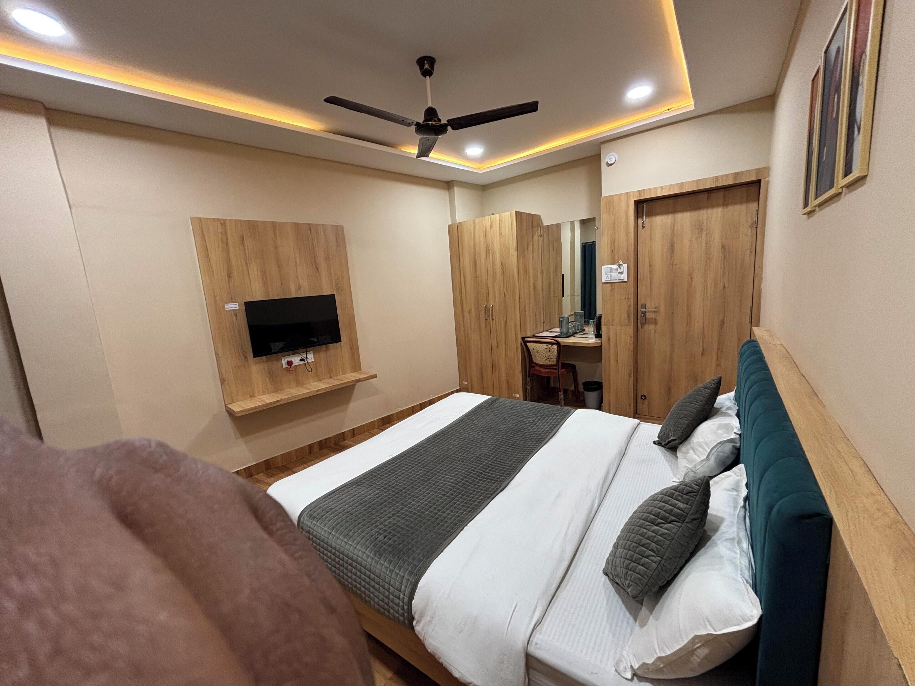 Een slaapkamer met een bed, een aan de muur bevestigde televisie, een plafondventilator en houten kasten.