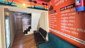 A hotel corridor with a mural of a sunset and palm trees, a staircase, and a seating area with a blue cushion. - Hotel Bhavya Ujjain (Ujjain)