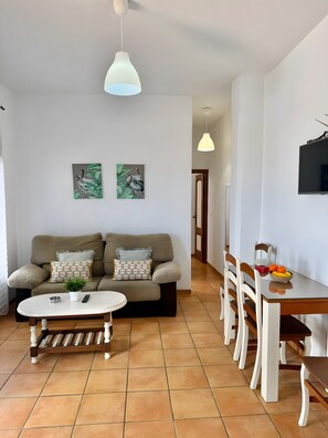 Ein Wohnzimmer mit Sofa, Couchtisch und Essbereich mit Stühlen sowie einem Fernseher.