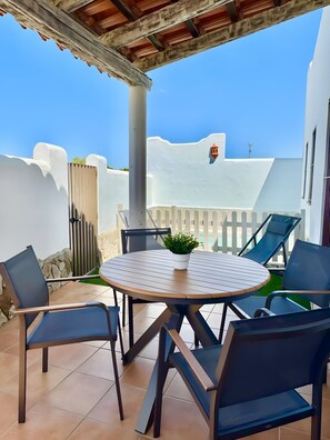 Eine Terrasse mit rundem Tisch, Stühlen und einem Blumentopf.