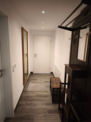 A hallway with a wooden floor, a white door at the end, and a mirror on the right. - Holiday Home 'Haus Am Deich' with Terrace, Private Garden & Wi-Fi (Norden)