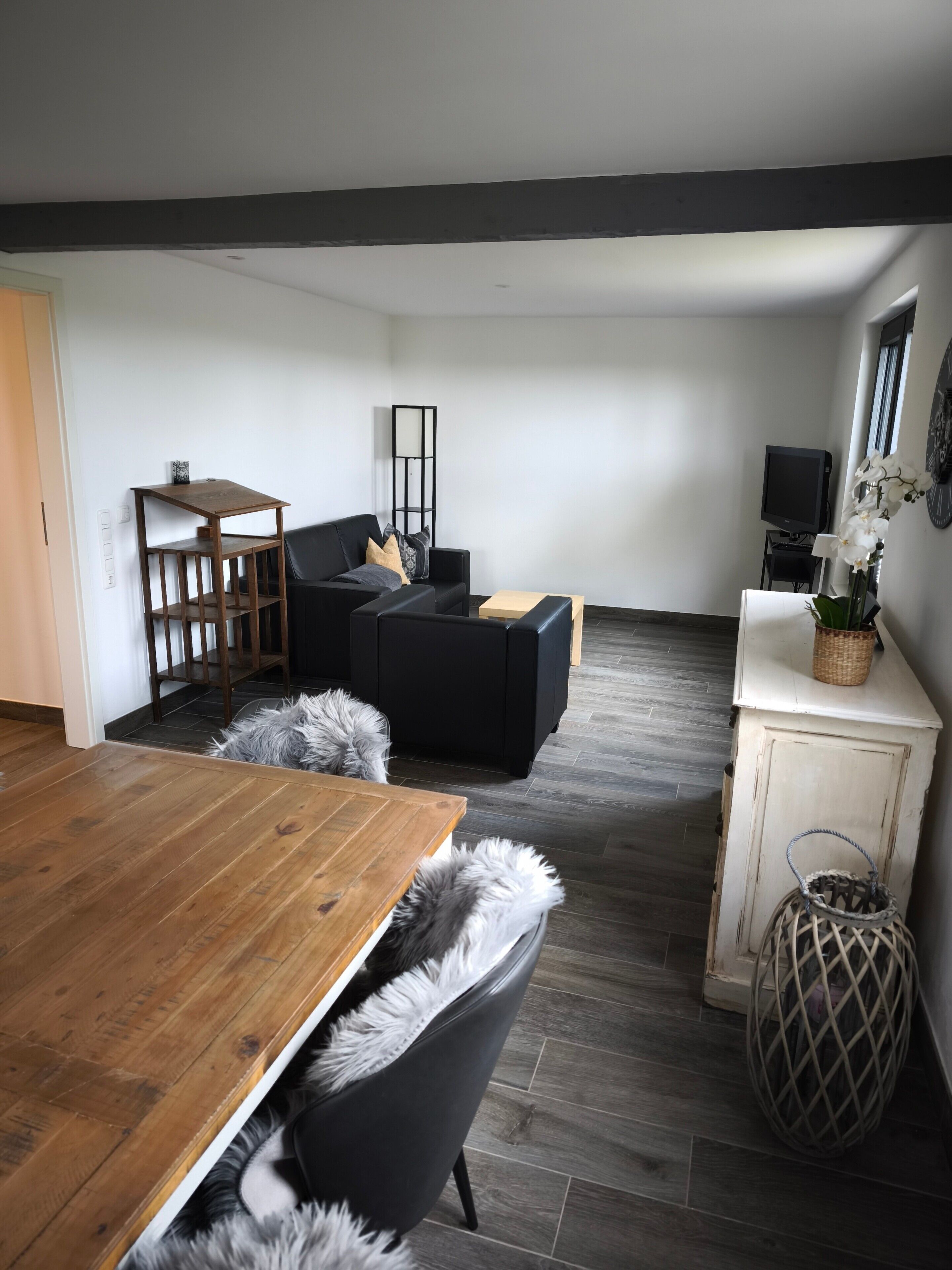 Ein modernes Wohnzimmer mit einem Holzesstisch, schwarzen Sofas, einem kleinen Fernseher und einer Zierpflanze.