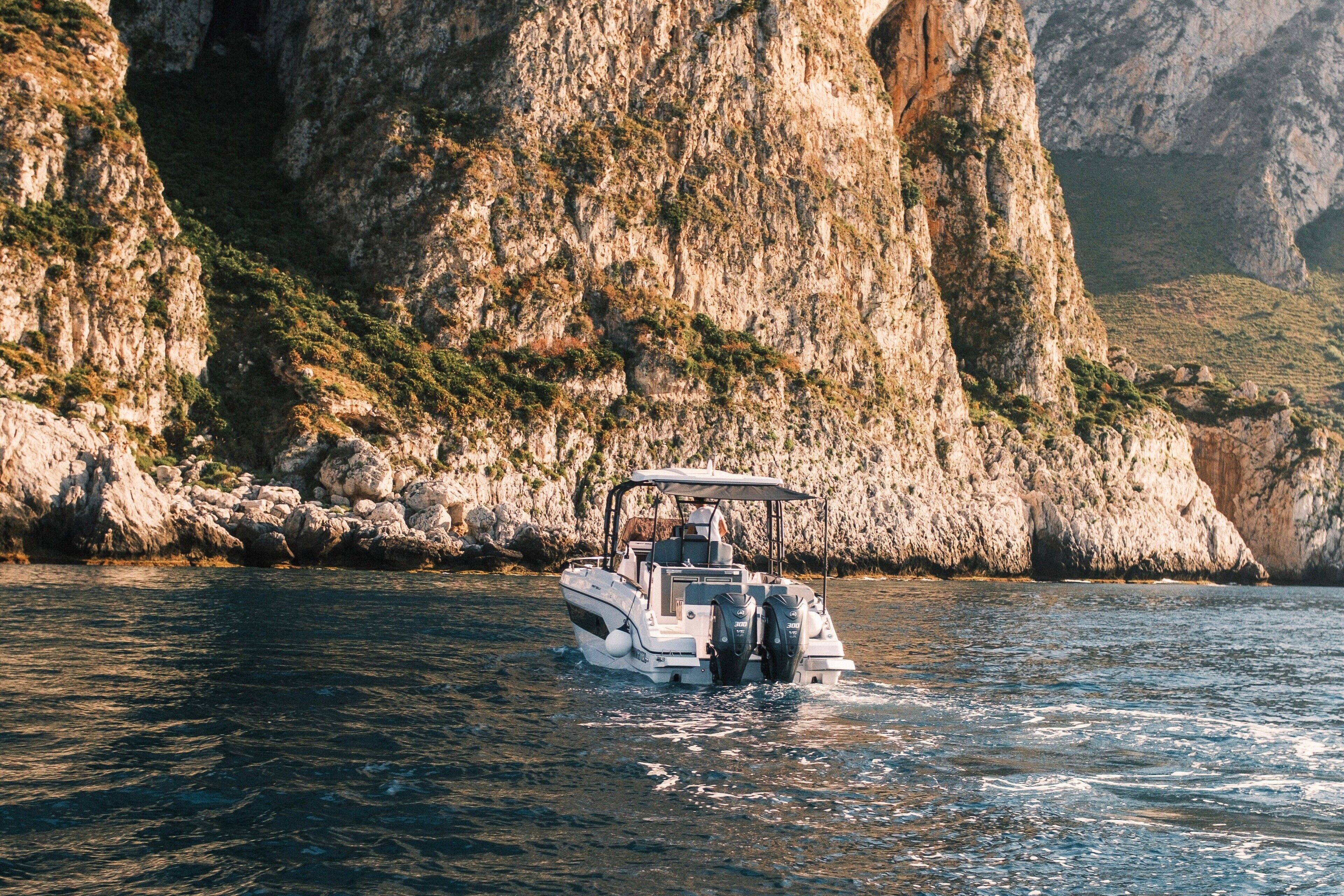 A boat on calm water with rocky cliffs in the background.