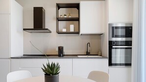 Una cocina moderna con armarios blancos, horno empotrado y una planta en maceta sobre la mesa.