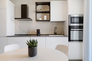 Una cocina moderna con armarios blancos, horno empotrado y una planta en maceta sobre la mesa.