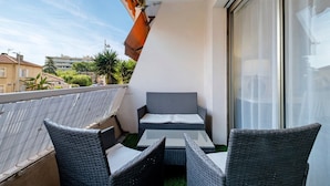A balcony with wicker furniture, a glass door, and a view of buildings and trees. - Apartment 'Couronne Du Cros' with Sea View, Wi-Fi and Air Conditioning (Cagnes-sur-Mer)