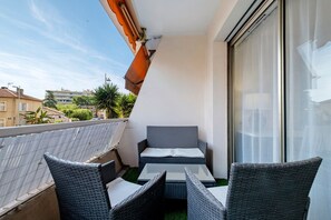 Een balkon met rieten meubels, een glazen deur en uitzicht op gebouwen en bomen.