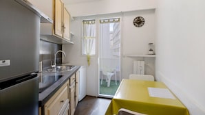 A compact kitchen with a stainless steel refrigerator, a sink, and a dining area with a yellow table. - Apartment 'Couronne Du Cros' with Sea View, Wi-Fi and Air Conditioning (Cagnes-sur-Mer)
