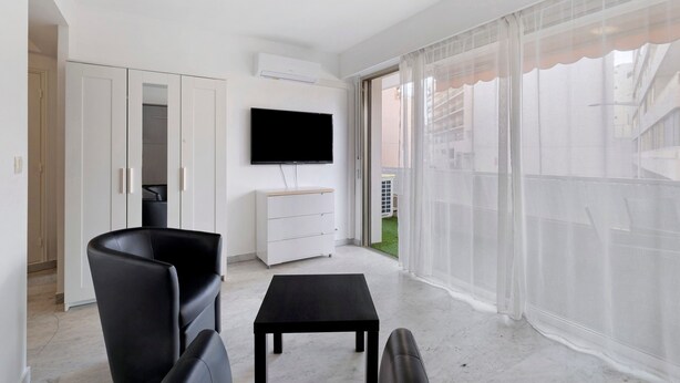 A modern living room with a flat-screen TV, a black leather chair, a small black table, and a white cabinet. - Apartment 'Couronne Du Cros' with Sea View, Wi-Fi and Air Conditioning (Cagnes-sur-Mer)