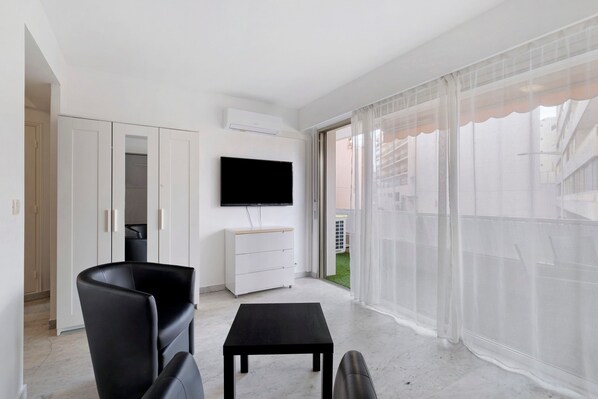 Een moderne woonkamer met een flatscreentelevisie, een zwarte leren fauteuil, een klein zwart tafeltje en een witte kast.